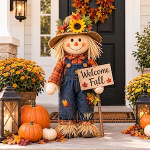 May include: A decorative scarecrow figure wearing a straw hat adorned with a sunflower and autumn leaves, a plaid shirt, and denim overalls. The figure holds a wooden sign that reads Welcome Fall with red maple leaf accents on the sign.