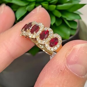 Peut inclure: Une bague en or orn&eacute;e de quatre pierres pr&eacute;cieuses rouge fonc&eacute; de taille ovale dispos&eacute;es en rang&eacute;e. Chaque pierre rouge est entour&eacute;e d'un halo de petites pierres claires et scintillantes serties sur l'anneau en or.