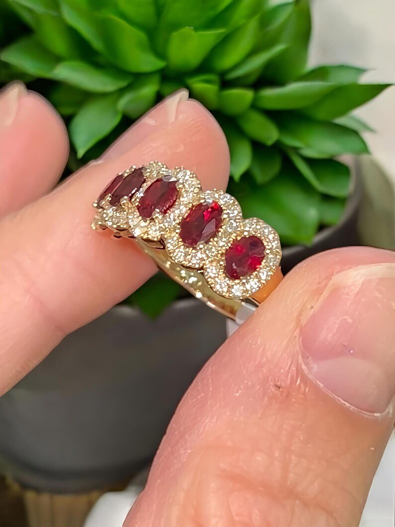 Peut inclure: Une bague en or orn&eacute;e de quatre pierres pr&eacute;cieuses rouge fonc&eacute; de taille ovale dispos&eacute;es en rang&eacute;e. Chaque pierre rouge est entour&eacute;e d'un halo de petites pierres claires et scintillantes serties sur l'anneau en or.