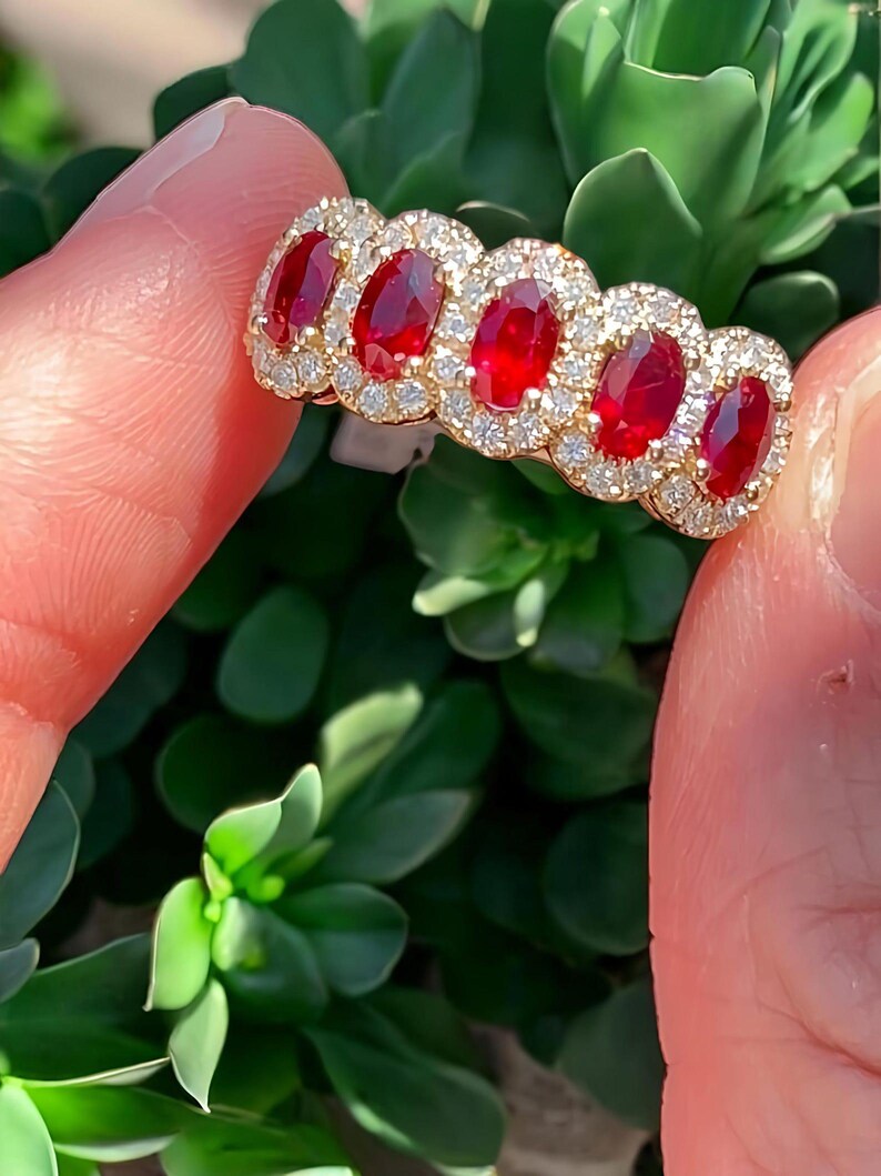Peut inclure: Une bague en or orn&eacute;e de cinq rubis rouges taille ovale dispos&eacute;s en rang&eacute;e, chacun entour&eacute; d'un halo de petits diamants blancs ronds et clairs. L'anneau est en or jaune poli, mettant en valeur un contraste vibrant entre les pierres pr&eacute;cieuses rouge profond et les accents &eacute;tincelants des diamants blancs.