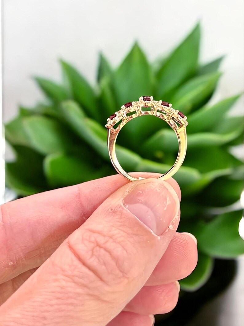 Peut inclure: Une bague en or orn&eacute;e d'une rang&eacute;e de cinq petites pierres pr&eacute;cieuses rondes d'un rouge profond, serties le long de l'anneau sup&eacute;rieur. L'anneau en m&eacute;tal est poli et lisse, pr&eacute;sentant un sertissage &agrave; griffes classique pour chaque pierre.