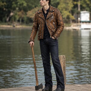 May include: A brown snakeskin-patterned leather motorcycle jacket with silver zippers and lapels, worn over a dark navy polo shirt and dark blue denim jeans, paired with black leather boots and holding a wooden-handled metal axe.