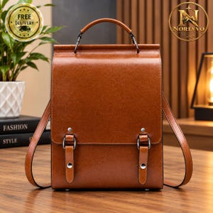 Peut inclure: Un sac à dos structuré de couleur marron avec une finition lisse, doté d'une poignée supérieure, de deux bretelles réglables et d'un rabat avant sécurisé par deux sangles verticales à boucle avec des ferrures et rivets en métal argenté.