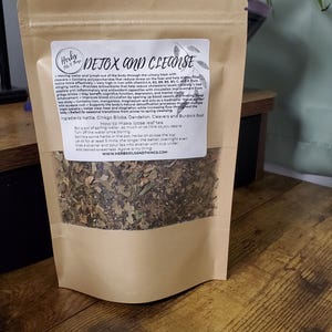 May include: A brown stand-up pouch containing loose leaf tea with a clear window. The white label features the text Detox and Cleanse, a list of ingredients including Nettle, Ginkgo Biloba, Dandelion, Cleavers, and Burdock Root, and instructions.