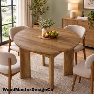 May include: A round wooden dining table with a natural grain finish and three thick, sturdy legs. Four chairs with light beige upholstered seats and wooden frames are positioned around the table. A woven placemat holds a vase and a bowl of green apples.