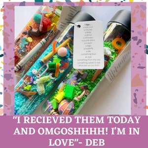 May include: Three clear plastic bottles filled with colorful rice and small objects. The bottles are labeled with the text "I Spy..." and a list of items to find. The bottles are a fun and engaging sensory toy for children.