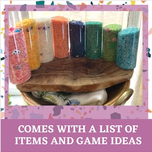 May include: Eight clear glass jars filled with different colored rice. The jars are lined up on a wooden surface.  Comes with a list of items and game ideas.