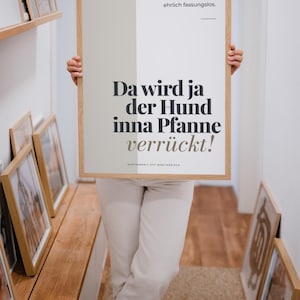 Könnte beinhalten: Ein rechteckiges gerahmtes Wandbild mit hellbeigem und weißem Hintergrund und schwarzem deutschem Text: Nr. 12, Ich bin gerade ehrlich fassungslos, Da wird ja der Hund inna Pfanne verrückt!, sowie ACHTSAMKEIT UFF BERLINERISCH in der unteren Zeile.
