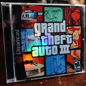 May include: A clear plastic jewel case for the Grand Theft Auto III video game for the Sega Dreamcast console. The cover art features a multi-panel comic book style collage of characters, a police helicopter, and a car with the ESRB M rating.