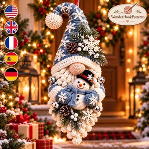 May include: A crochet gnome ornament featuring a blue hat with white snowflake patterns, a cream-coloured beard, and a small snowman figure. The gnome is decorated with pine branches, pinecones, white berries, and silver jingle bells.