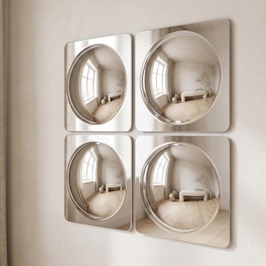 May include: A set of four square wall mirrors, each featuring a circular, concave center that creates a fisheye reflection. The mirrors have smooth, reflective surfaces and rounded corners, arranged in a two-by-two grid on a plain wall.