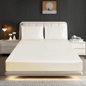 May include: A bed featuring a smooth, cream-coloured fitted sheet and two matching cream-coloured pillowcases. The bed has a white upholstered headboard with vertical paneling, positioned against a dark grey wall in a bedroom setting.