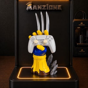 May include: A display stand featuring a yellow and blue gauntlet-style hand holding a white game controller with three silver claws extending upward. The base is black with an orange light border and the text MANZIONE with a crown icon at the top.