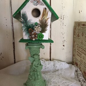 Beautiful embellished green and white decorative birdhouse on a candlestick.