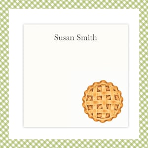 May include: A square white notepad featuring the name Susan Smith printed in dark gray text at the top and a detailed illustration of a golden-brown lattice-top pie in the bottom right corner, framed by a green and white gingham border.