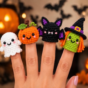 May include: A set of four crocheted finger puppets featuring a white ghost, an orange pumpkin with a green stem, a black bat with purple inner ears and white fangs, and a green witch with orange hair wearing a black hat with a purple band.