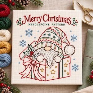 May include: A needlepoint pattern on white fabric featuring a gnome with a long beard and a striped hat inside a gift box. The text Merry Christmas Needlepoint Pattern is stitched in red and green. Blue snowflakes surround the central design.