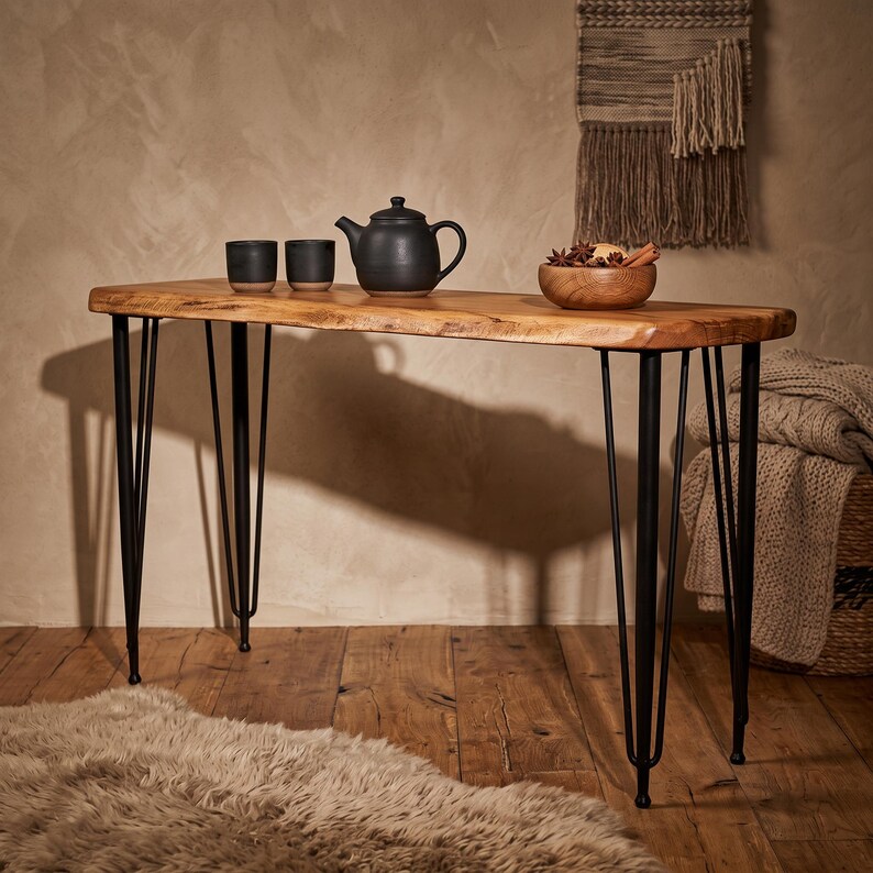 May include: A rectangular console table with a natural live-edge wood top and four black metal hairpin legs. On the surface sits a black teapot, two small black cups, and a wooden bowl containing star anise and cinnamon sticks.