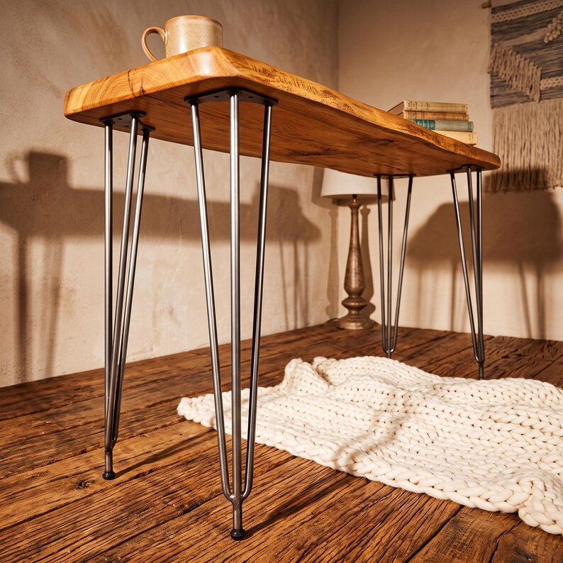 May include: A rectangular wooden desk featuring a natural live edge finish on the tabletop and four sets of slender, silver-toned metal hairpin legs. The desk surface displays a warm, light brown wood grain pattern with visible knots and texture.