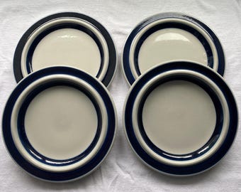 May include: Four ceramic plates with a cream-colored center and a dark blue border. The plates have a simple, modern design, suitable for everyday use or special occasions. The plates are arranged in a square formation.