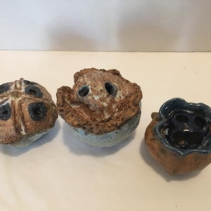 May include: Three ceramic flower pots with unique designs. The first pot is brown with black accents and a starburst pattern. The second pot is brown with blue accents and a textured surface. The third pot is brown with blue accents and a flower-like design.