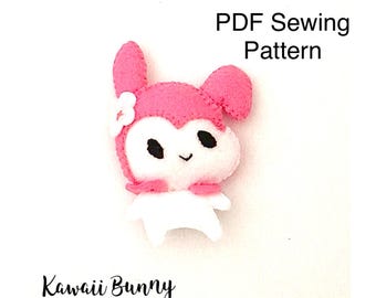 May include: A felt craft project featuring a white and pink bunny character with black eyes, a small smile, and a white flower accessory on its head. The text PDF Sewing Pattern and Kawaii Bunny are printed on the white background.
