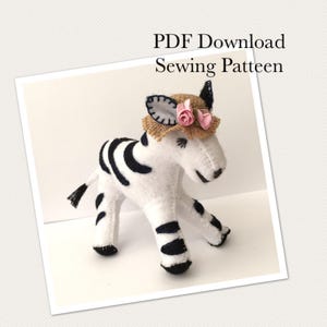 May include: A white and black felt zebra figurine wearing a tan straw hat adorned with two small pink fabric roses. The text PDF Download Sewing Patteen is visible at the top of the image, featuring stitched details on the zebra's body.
