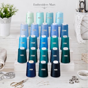 May include: A collection of twenty-one spools of embroidery thread arranged in a tiered display. Each spool features a unique blue or teal shade, labeled with codes such as P110, P091, P7089, P7132, P7075, P062, P7028, P061, P7133, P095, P7295, P096, P274, P101, P071, P7291, P108, P072, P098, P325, P7376, and P070. The brand name Embroidery Mart is printed at the top.