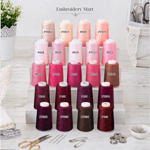 May include: A collection of twenty-four embroidery thread spools arranged in rows on a tiered white wooden stand. The spools feature various shades of pink, red, and brown, each labeled with a specific code. Embroidery Mart is printed at the top.