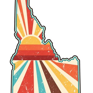 May include: A sticker shaped like the state of Idaho featuring a distressed graphic design. The interior displays a sunburst pattern with alternating stripes of red, orange, yellow, and teal, all enclosed within a bold black outline border.
