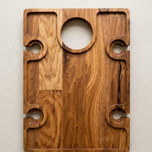 May include: A rectangular wooden serving board featuring a natural brown grain pattern. The board includes a circular cutout at the top center and four semi-circular notches along the side edges, designed to hold items securely in place.