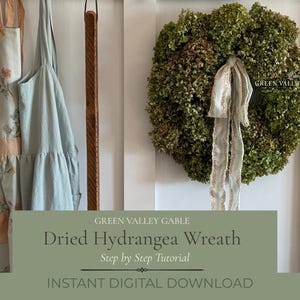 May include: A round wreath made of dried green hydrangea flowers featuring a long, light blue patterned ribbon hanging from the center. To the left, two aprons hang, one with a floral print and peach pocket, the other solid light blue.