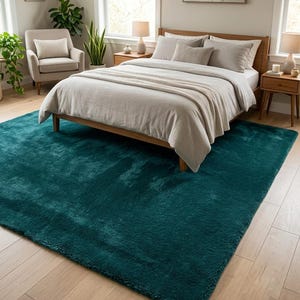 Peut inclure: Un grand tapis rectangulaire d'une couleur sarcelle profonde et unie, doté d'une texture épaisse, moelleuse et à poils longs. Le tapis est placé sur un sol en bois clair, s'étendant sous un cadre de lit en bois avec une parure de lit neutre.