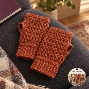 May include: A pair of burnt orange fingerless gloves featuring a textured crochet stitch pattern and ribbed cuffs. A circular inset in the corner displays a small octopus toy and the text FREE GIFT.