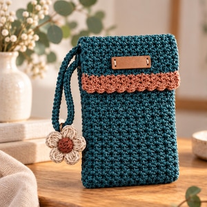May include: A teal crochet phone pouch featuring a textured star stitch pattern, a scalloped peach-coloured trim, and a rectangular brown leather label. A matching teal wrist strap is attached, adorned with a small, six-petaled beige flower charm.
