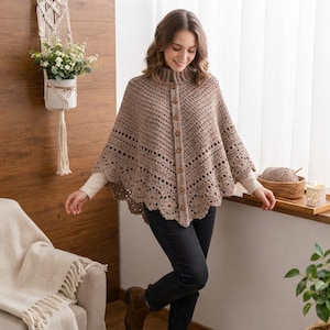 Può includere: Un poncho all'uncinetto color marrone chiaro con collo alto, una fila verticale di bottoni in legno al centro e un orlo smerlato decorativo. Il capo è realizzato con un motivo a maglia testurizzato e viene indossato sopra una maglia a maniche.