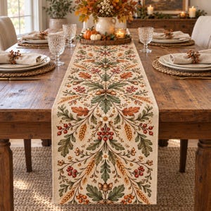 May include: A rectangular table runner featuring a repeating botanical pattern of green oak leaves, orange autumn foliage, red berries, wheat stalks, and brown acorns on a cream-colored fabric base, centered on a wooden dining table.