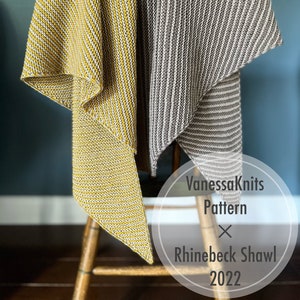 Pode incluir: Dois xales de malha listrados, um amarelo e branco, o outro cinza e branco, drapeados sobre uma cadeira de madeira. Os xales são etiquetados como "VanessaKnits Pattern x Rhinebeck Shawl 2022".