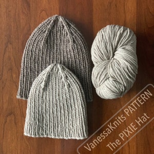 May include: Two knitted hats in beige and brown, with a ball of beige yarn. The hats are made with a simple stitch pattern and have a slouchy fit. The yarn is labeled "VanessaKnits PATTERN The PIXIE Hat."