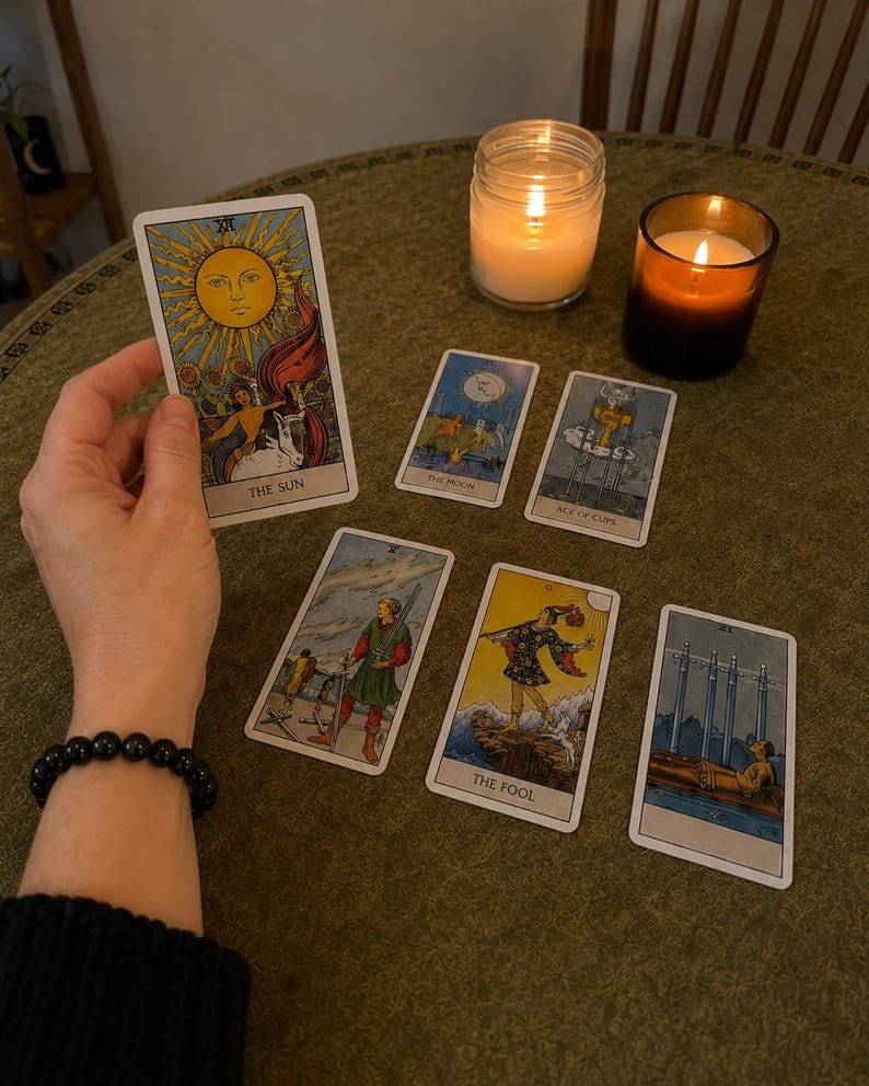Hand holding The Sun tarot card above a tarot spread with lit candles, psychic tarot reading by intuitive reader Liora