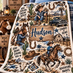 Op de afbeelding: Een zachte fleece deken met een western thema, voorzien van illustraties van een kind met een cowboyhoed, paarden, een pick-up truck, cactussen en een houten bord met de naam Hudson. Tekst bevat Ride Explore Dream Repeat en Adventure Awaits.
