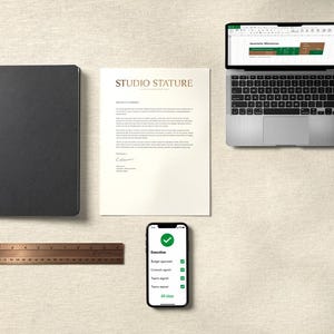 May include: A black notebook, a white letterhead with the text STUDIO STATURE, a silver laptop displaying a spreadsheet, a copper ruler measuring 12 inches, and a smartphone showing a green checkmark and a list of tasks labeled Executive.