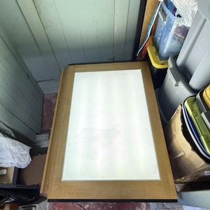 May include: A rectangular light box featuring a bright white illuminated panel centered within a natural wood-toned frame. The device emits a uniform glow across its surface, providing a flat, backlit area for viewing or tracing tasks.