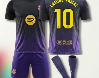 Puede incluir: Un conjunto de fútbol negro y morado con el nombre LAMINE YAMAL y el número 10 en amarillo en la parte posterior. La camiseta incluye un logo de Spotify, un escudo de equipo y el logo de UNHCR ACNUR. El set incluye pantalones y medias.