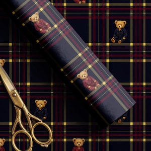 May include: A roll of navy blue wrapping paper featuring a repeating plaid pattern of thin red and yellow lines, interspersed with small illustrations of teddy bears wearing either red or navy blue pajamas, alongside gold-toned metal scissors.