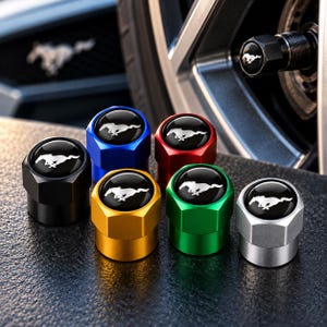 May include: A set of six hexagonal tire valve stem caps in black, blue, red, gold, green, and silver. Each cap features a circular black insert on top with a white galloping horse emblem. One cap is shown installed on a vehicle wheel valve stem.