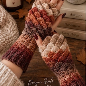 May include: A pair of fingerless gloves featuring a textured dragon scale crochet pattern in a gradient of autumn colors including cream, orange, rust, and dark brown. The gloves have a ribbed cuff and extend to the knuckles with a scale design.