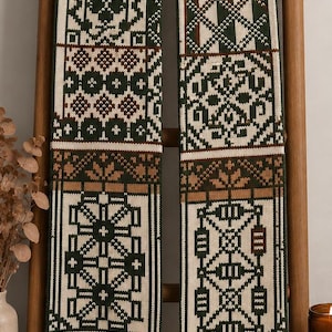 Könnte beinhalten: Ein langer Strickschal mit einem sich wiederholenden geometrischen Muster in Waldgrün, Creme und Hellbraun. Das Design besteht aus gestapelten rechteckigen Feldern mit komplexen, symmetrischen Motiven, einschließlich sternartiger Formen.