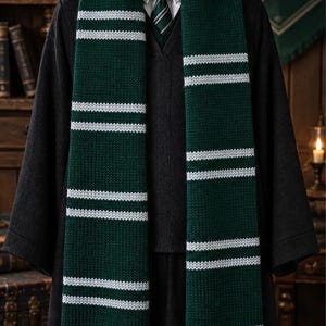 Könnte beinhalten: Ein gestrickter Schal mit dunkelgrüner Basis und horizontalen weißen Streifen, drapiert über einem dunkelgrauen V-Ausschnitt-Pullover, einem weißen Hemd mit Kragen und einer grün-weiß gestreiften Krawatte. Der Schal hat ein Strickmuster und Fransen.