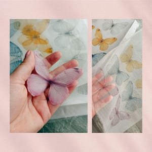 May include: A delicate, translucent, pink butterfly is held in a hand, with a sheet of paper featuring various butterfly designs in the background. The butterflies on the paper are in shades of yellow, blue, and white.